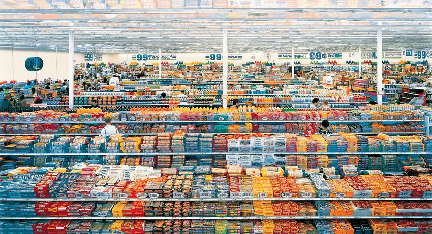 Andreas Gursky, 99 Cent: toàn cảnh nội thất siêu thị đồng giá, các dãy kệ hàng hoá nhiều màu kéo dài dưới trần bóng