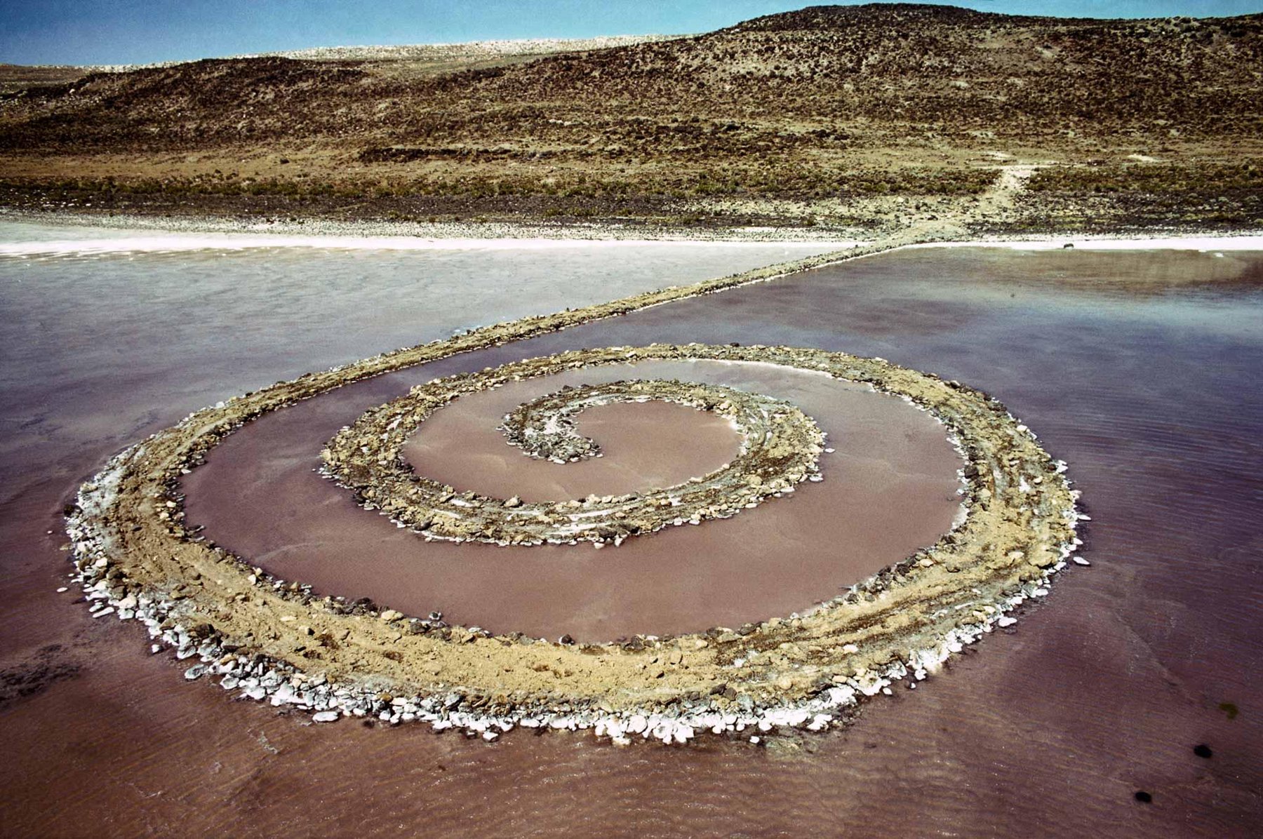ロバート・スミッソン「Spiral Jetty」：ユタ州グレートソルト湖の水へと巻き込む黒い玄武岩と土の螺旋、上空から