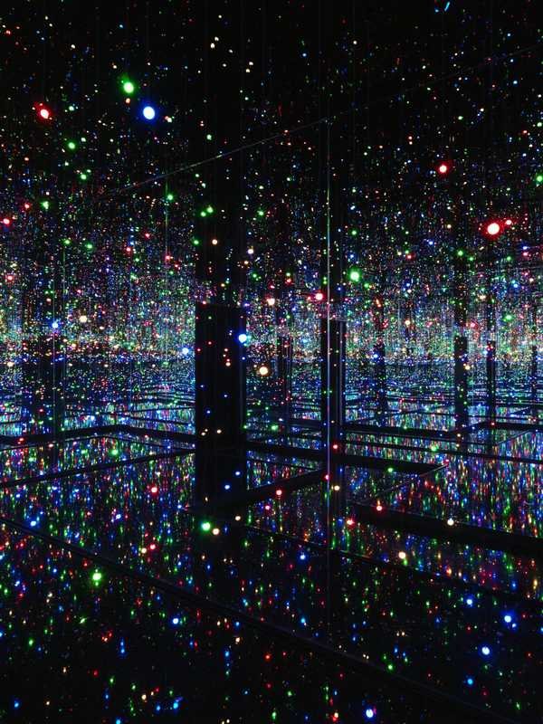 草間彌生「Infinity Mirrored Room: Filled with the Brilliance of Life」。水の上の通路と、鏡の部屋で果てしなく映り込む数百の小さな色の光